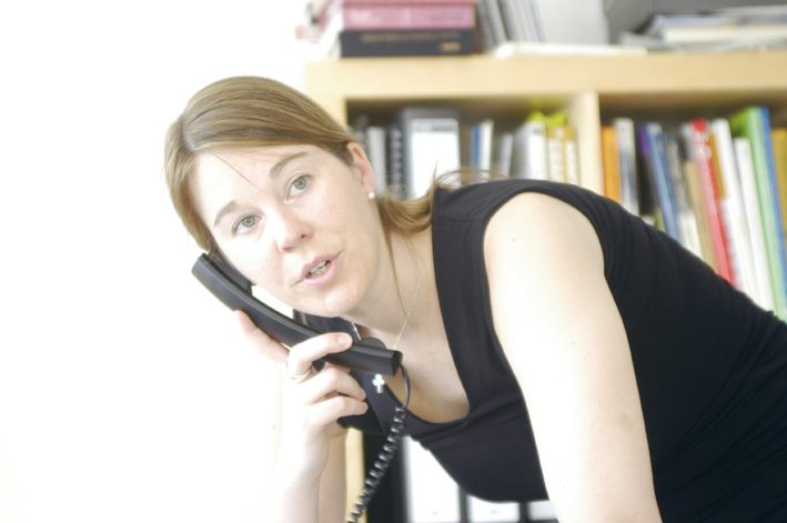 Petra on the phone at her desk in front of a bookshelf